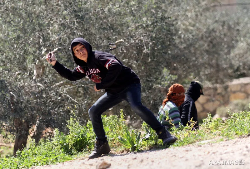 A Palestinian protester uses a slingshot to hurl stones towards Israeli security forces during clashes following a demonstration against the expropriation of Palestinian land by Israel on February 19, 2016 in the village...