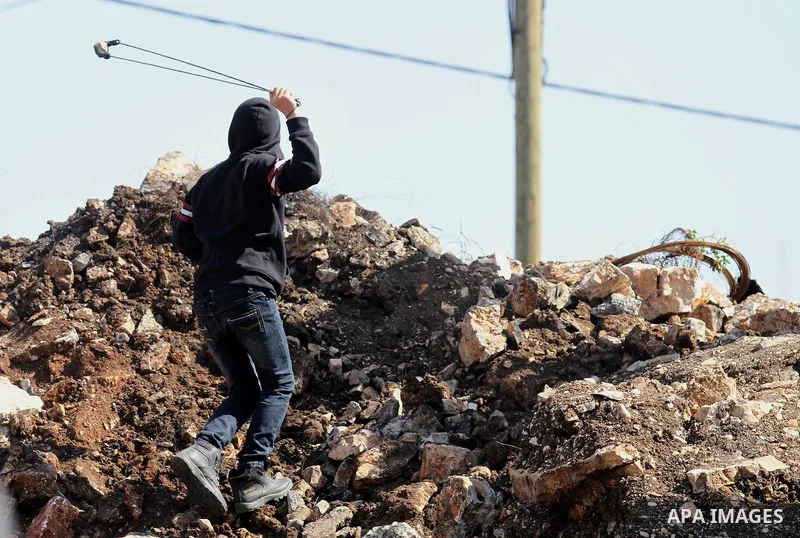 A Palestinian protester uses a slingshot to hurl stones towards Israeli security forces during clashes following a demonstration against the expropriation of Palestinian land by Israel on February 19, 2016 in the village...