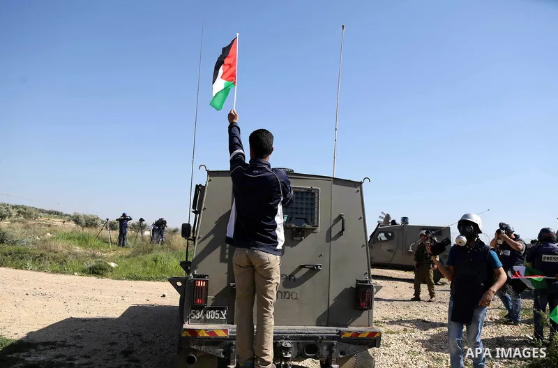 A Palestinian man puts a national flag atop a vehicle of Israeli security forces during clashes following a march on February 19, 2016 in the West Bank village of Bilin, near Ramallah, to mark the 11th anniversary of the...