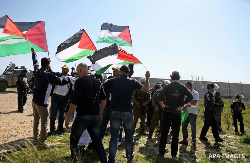 Palestinians hold national flags during clashes with Israeli security forces following a march on February 19, 2016 in the West Bank village of Bilin, near Ramallah, to mark the 11th anniversary of their uprising against...