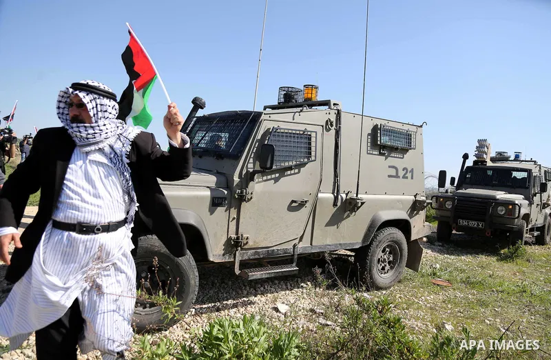 A Palestinian man holds national flags during clashes with Israeli security forces following a march on February 19, 2016 in the West Bank village of Bilin, near Ramallah, to mark the 11th anniversary of their uprising a...