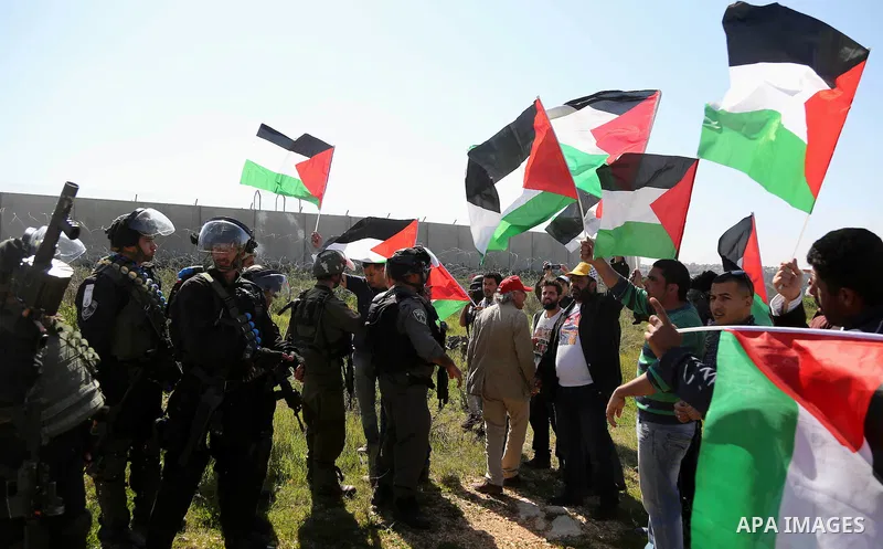 Palestinians hold national flags during clashes with Israeli security forces following a march on February 19, 2016 in the West Bank village of Bilin, near Ramallah, to mark the 11th anniversary of their uprising against...