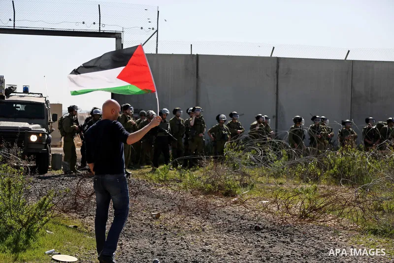A Palestinian man holds national flags during clashes with Israeli security forces following a march on February 19, 2016 in the West Bank village of Bilin, near Ramallah, to mark the 11th anniversary of their uprising a...