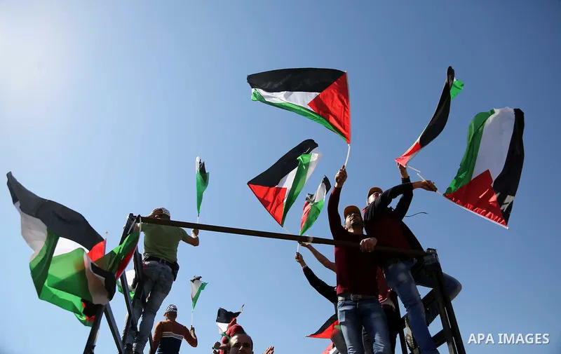 Palestinians hold national flags during clashes with Israeli security forces following a march on February 19, 2016 in the West Bank village of Bilin, near Ramallah, to mark the 11th anniversary of their uprising against...