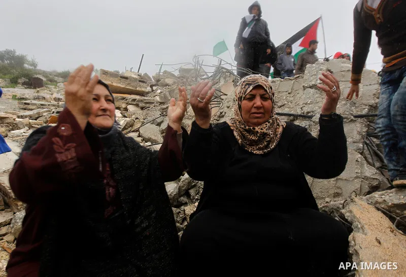 Palestinians warm themselves by a fire as they sit in front of the rubbles of Palestinian Raed Masalmeh's home after it was demolished by Israeli army in the West Bank town of Dura, south of Hebron February 23, 2016. Isr...