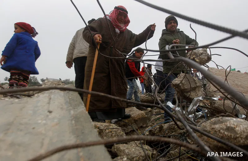 Palestinians warm themselves by a fire as they sit in front of the rubbles of Palestinian Raed Masalmeh's home after it was demolished by Israeli army in the West Bank town of Dura, south of Hebron February 23, 2016. Isr...