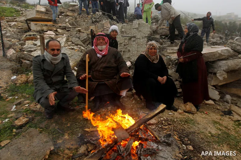 Palestinians warm themselves by a fire as they sit in front of the rubbles of Palestinian Raed Masalmeh's home after it was demolished by Israeli army in the West Bank town of Dura, south of Hebron February 23, 2016. Isr...