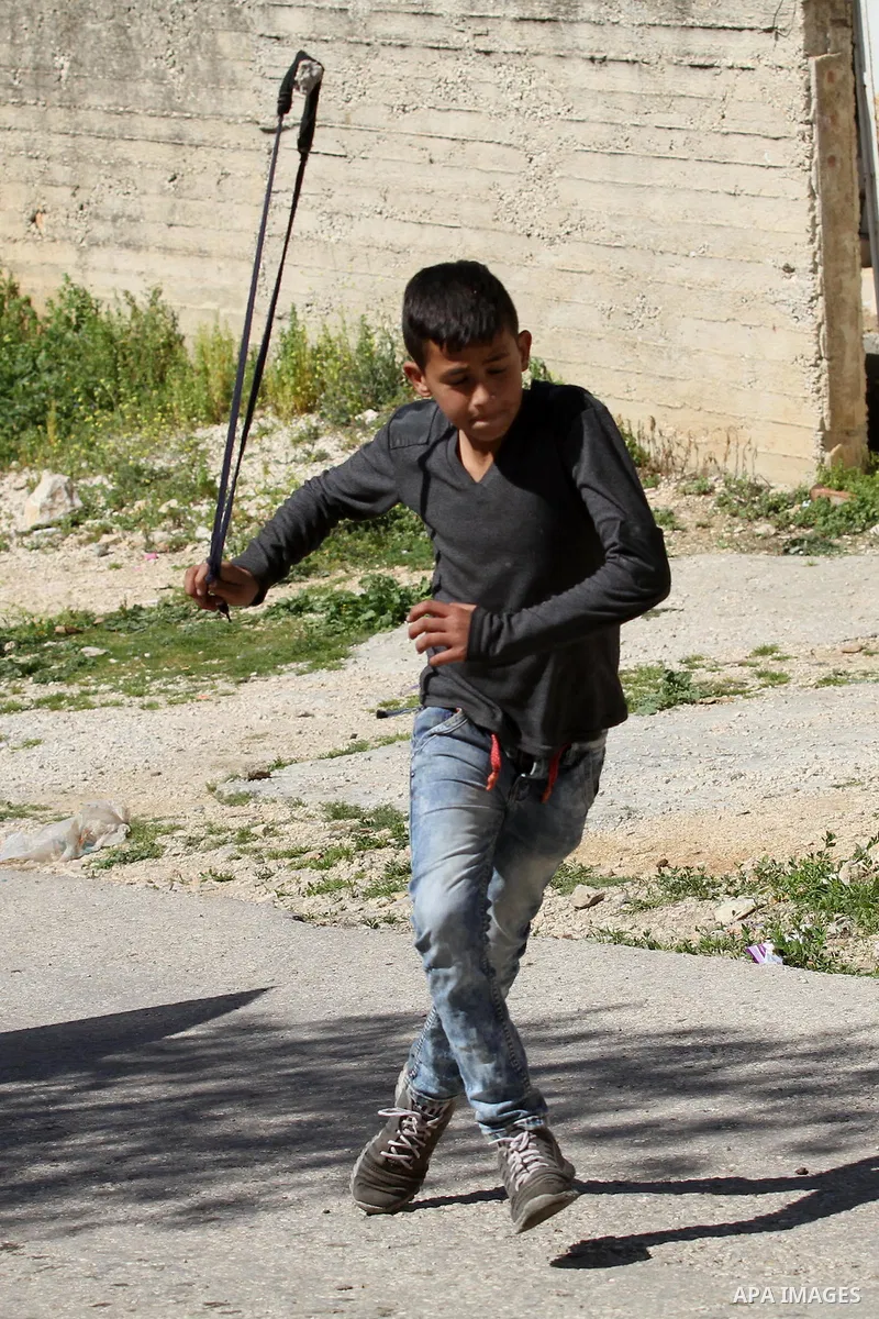 A Palestinian protester uses a slingshot to hurl stones toward Israeli security forces during clashes following a protest against the expropriation of Palestinian land by Israel in the West Bank village of Kafr Qaddum, n...