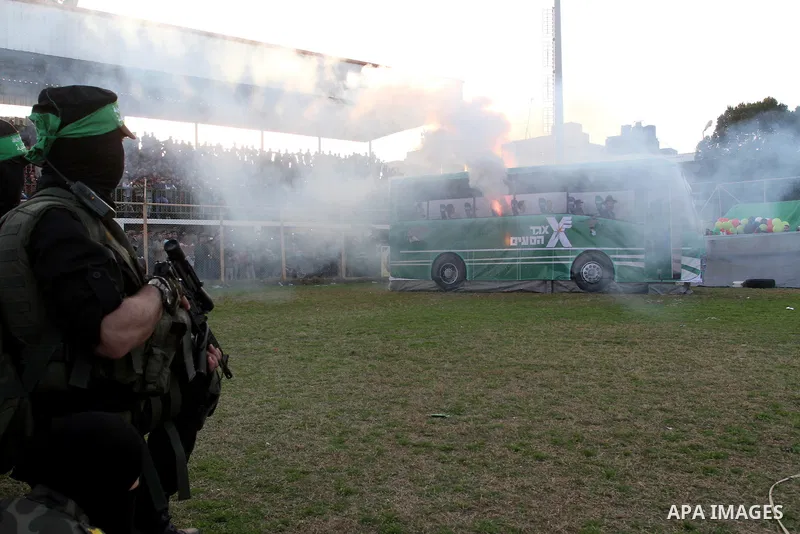 Palestinian militants of the Ezzedine al-Qassam Brigades, the armed wing of the Hamas movement, look at a mock bus burning during a show as part of an anti-Israel rally on February 26, 2016, in the southern Gaza Strip to...