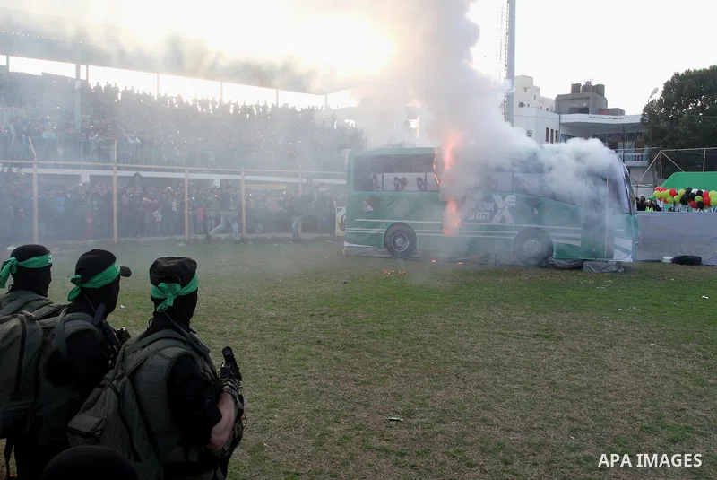 Palestinian militants of the Ezzedine al-Qassam Brigades, the armed wing of the Hamas movement, look at a mock bus burning during a show as part of an anti-Israel rally on February 26, 2016, in the southern Gaza Strip to...