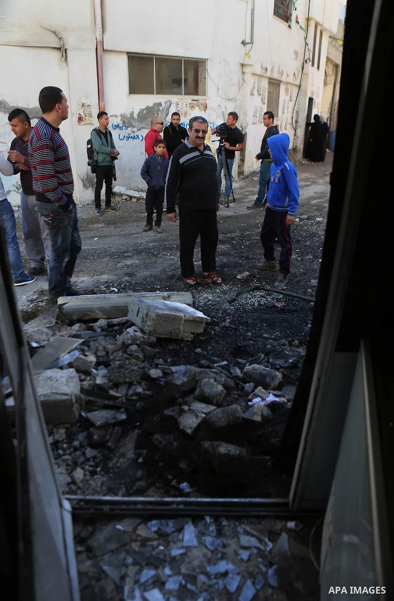 Palestinian men stand next to the charred remains of an Israeli military vehicle at the Qalandya Refugee camp following clashes between Palestinian youths and Israeli security forces on March 1, 2016. Two Israeli soldier...