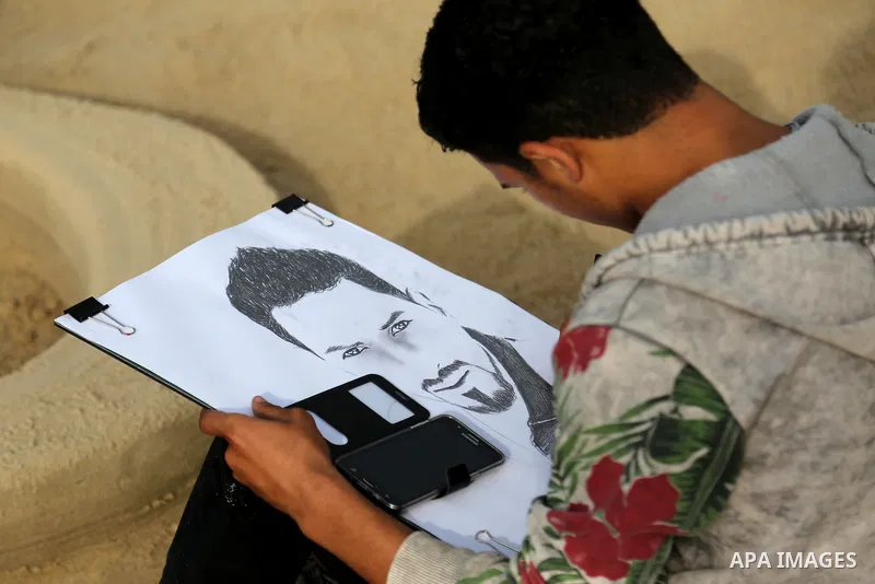 A Palestinian artist paints a portrait of Bahaa Alian, who was killed by Israeli security forces during a reading human chain at the beach of Gaza city on March 03, 2016. Photo by Mohammed Asad