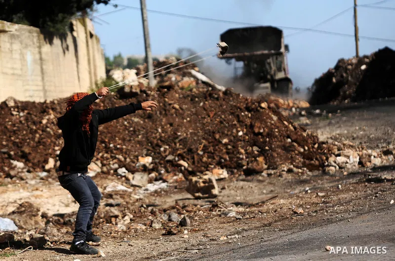 A Palestinian protester uses a slingshot to hurl stones toward Israeli security foces during clashes following a demonstration against the expropriation of Palestinian land by Israel in the village of Kfar Qaddum, near N...