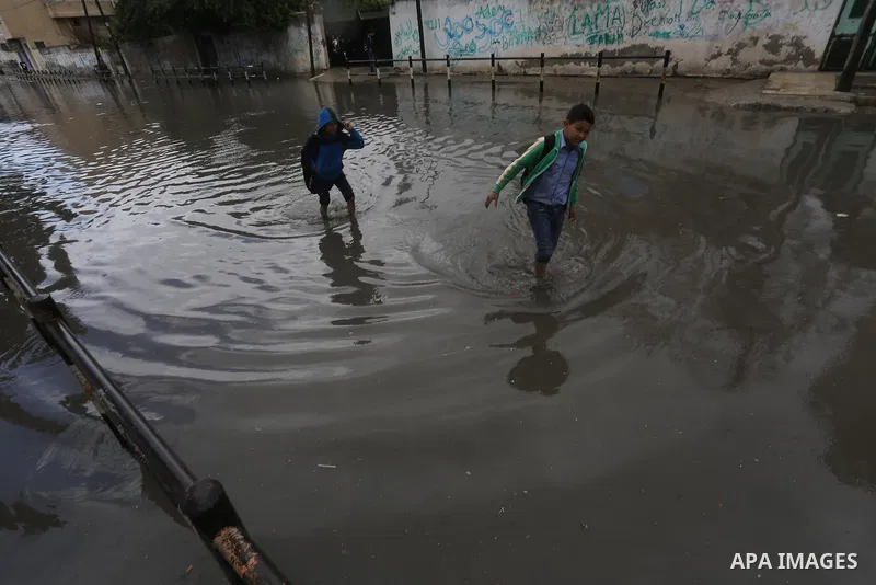 Palestinians walk in a street flooded by rain water, in Gaza city, on March 16, 2016. Photo by Mohammed Asad