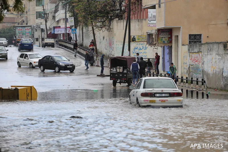 Palestinians walk in a street flooded by rain water, in Gaza city, on March 16, 2016. Photo by Mohammed Asad