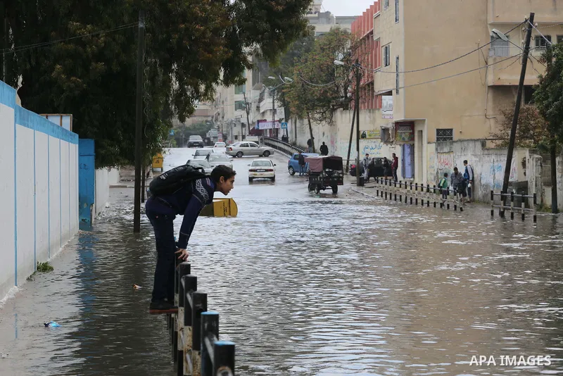Palestinians walk in a street flooded by rain water, in Gaza city, on March 16, 2016. Photo by Mohammed Asad