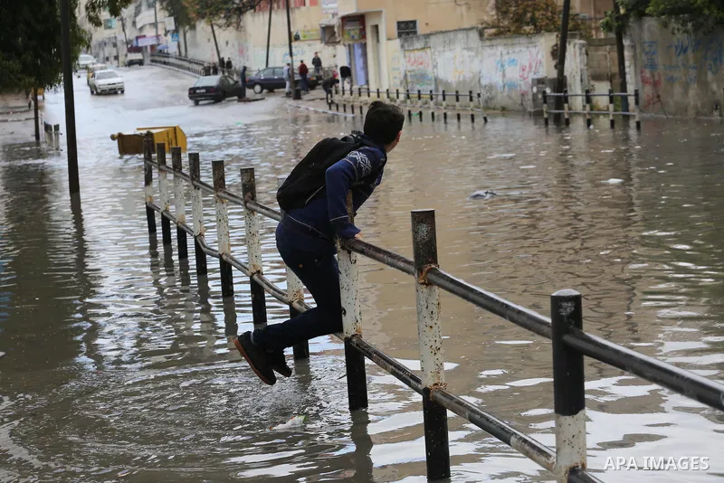 Palestinians walk in a street flooded by rain water, in Gaza city, on March 16, 2016. Photo by Mohammed Asad