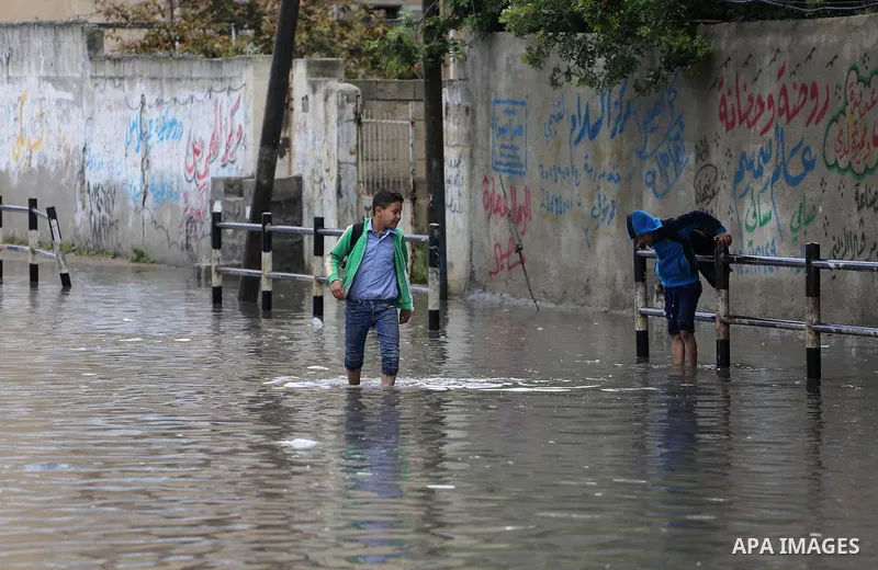 Palestinians walk in a street flooded by rain water, in Gaza city, on March 16, 2016. Photo by Mohammed Asad
