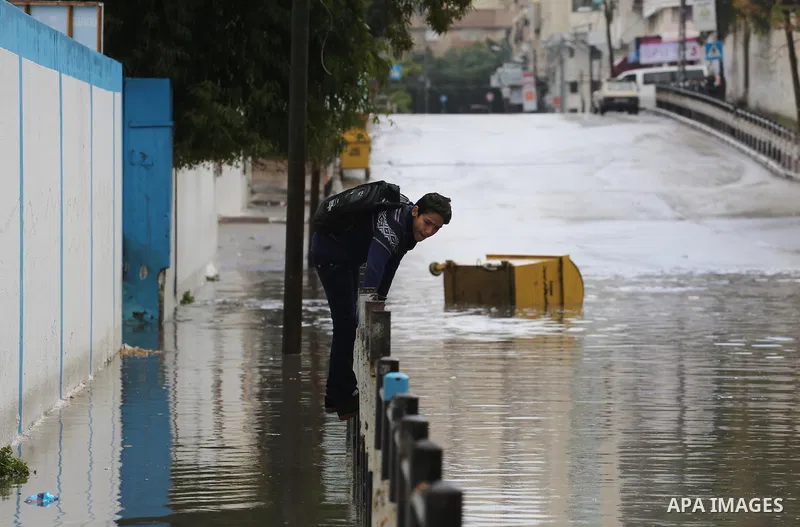 Palestinians walk in a street flooded by rain water, in Gaza city, on March 16, 2016. Photo by Mohammed Asad