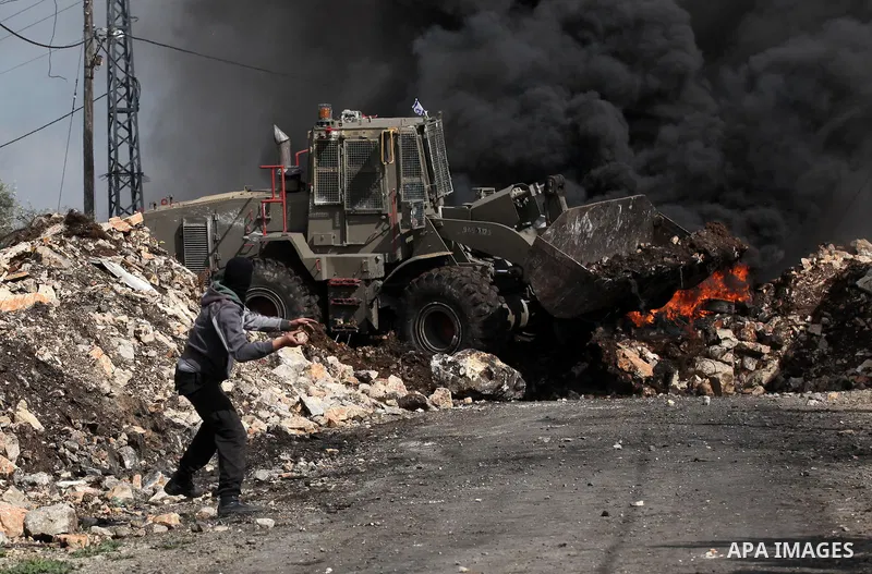 A Palestinian protester hurls stones at an Israeli military bulldozer during clashes following a demonstration against the expropriation of Palestinian land by Israel in the village of Kfar Qaddum, near Nablus, in the oc...