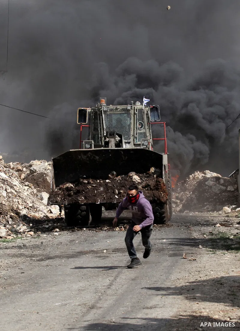 A Palestinian protester hurls stones at an Israeli military bulldozer during clashes following a demonstration against the expropriation of Palestinian land by Israel in the village of Kfar Qaddum, near Nablus, in the oc...