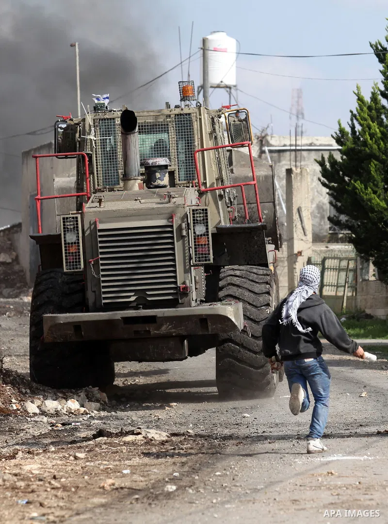 A Palestinian protester hurls stones at an Israeli military bulldozer during clashes following a demonstration against the expropriation of Palestinian land by Israel in the village of Kfar Qaddum, near Nablus, in the oc...