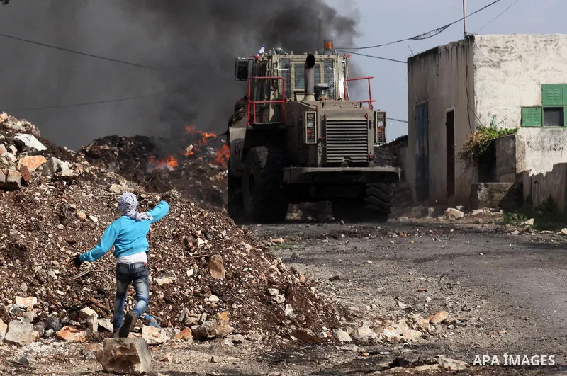 A Palestinian protester hurls stones at an Israeli military bulldozer during clashes following a demonstration against the expropriation of Palestinian land by Israel in the village of Kfar Qaddum, near Nablus, in the oc...