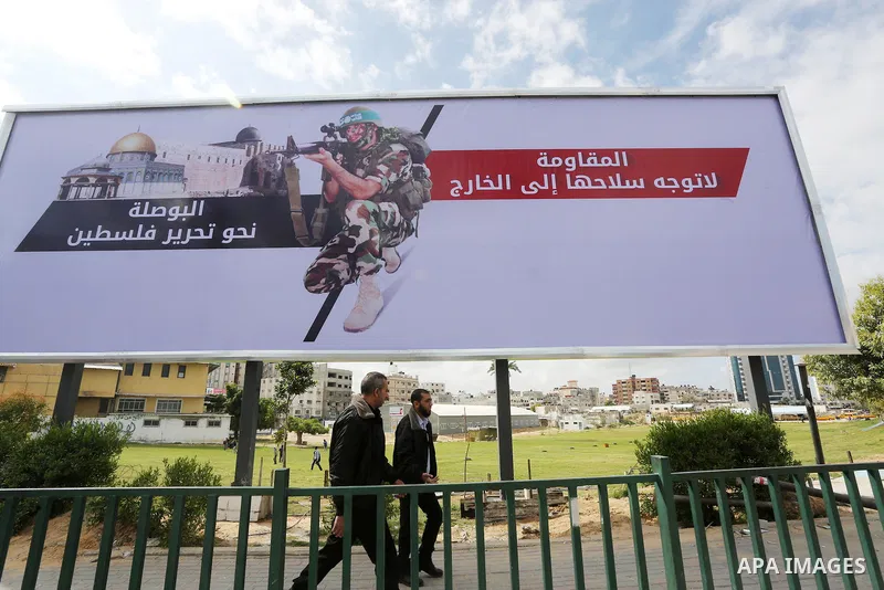 Palestinians walk past a placard depicting a member of the Ezzedine al-Qassam Brigades, the armed wing of the Hamas movement in Gaza city on March 20, 2016. Photo by Mohammed Asad