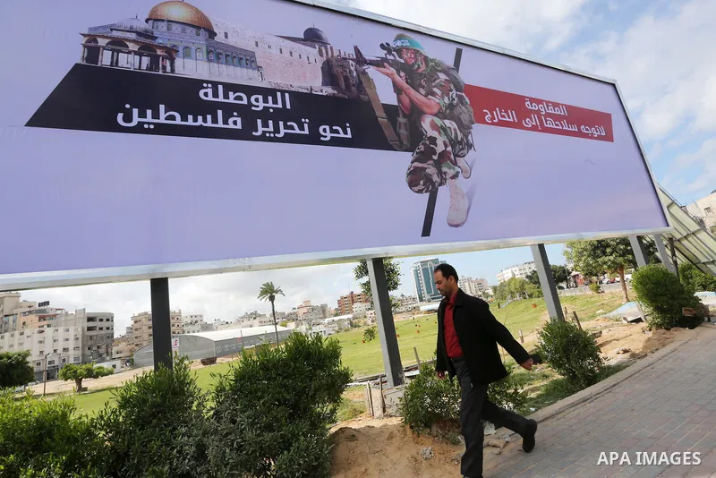 Palestinians walk past a placard depicting a member of the Ezzedine al-Qassam Brigades, the armed wing of the Hamas movement in Gaza city on March 20, 2016. Photo by Mohammed Asad
