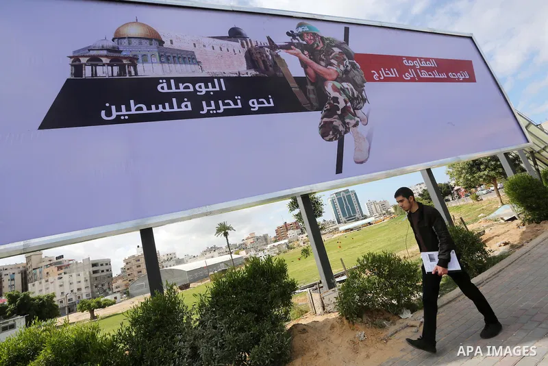 Palestinians walk past a placard depicting a member of the Ezzedine al-Qassam Brigades, the armed wing of the Hamas movement in Gaza city on March 20, 2016. Photo by Mohammed Asad