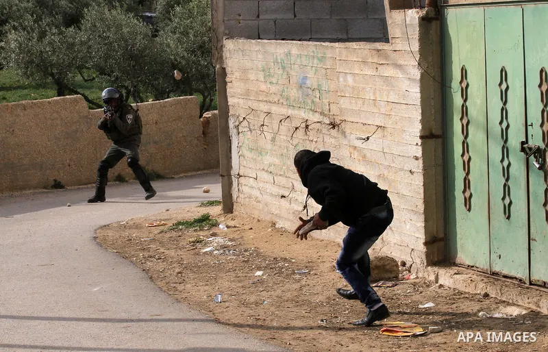 A Palestinian man throws stones towards an Israeli security member in the Israeli occupied West Bank village of Duma near Nablus, after fire broke out in the early hours of March 20, 2016 in the home belonging to a Pales...