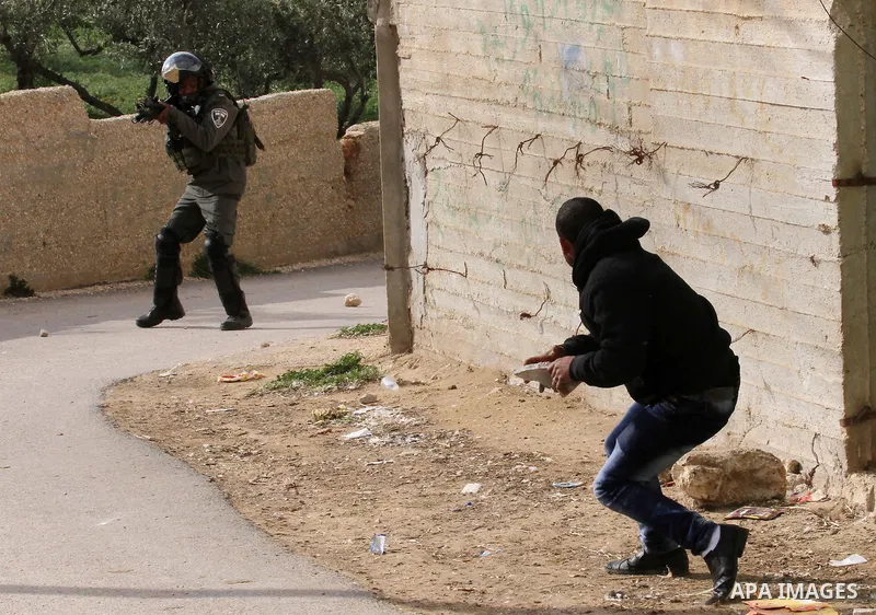 A Palestinian man throws stones towards an Israeli security member in the Israeli occupied West Bank village of Duma near Nablus, after fire broke out in the early hours of March 20, 2016 in the home belonging to a Pales...