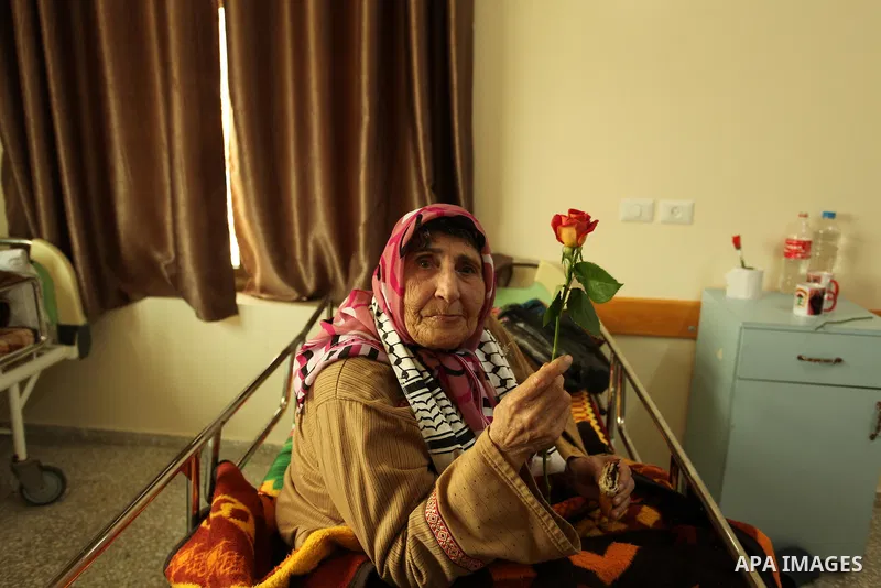 A Palestinian elderly woman holds flowers to mark the anniversary of Mother's Day, at Al-Wafa association for the elderly in Gaza city on March 21, 2016. Photo by Ashraf Amra
