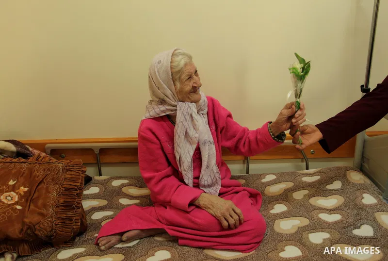 A Palestinian elderly woman holds flowers to mark the anniversary of Mother's Day, at Al-Wafa association for the elderly in Gaza city on March 21, 2016. Photo by Ashraf Amra