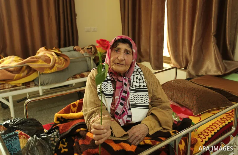 A Palestinian elderly woman holds flowers to mark the anniversary of Mother's Day, at Al-Wafa association for the elderly in Gaza city on March 21, 2016. Photo by Ashraf Amra