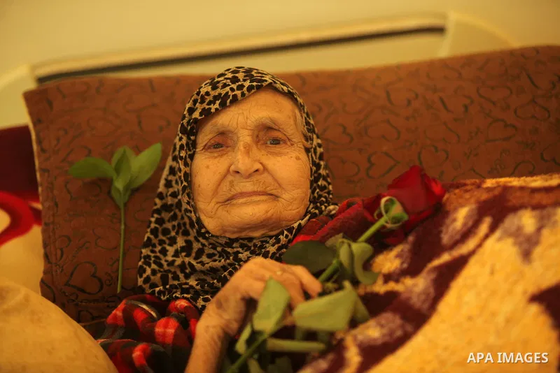 A Palestinian elderly woman holds flowers to mark the anniversary of Mother's Day, at Al-Wafa association for the elderly in Gaza city on March 21, 2016. Photo by Ashraf Amra