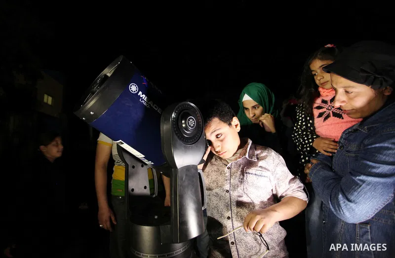 Palestinian children look through a telescope to watch the moon and stars at Al-qattan center in Gaza city on March 23, 2016. Photo by Ashraf Amra