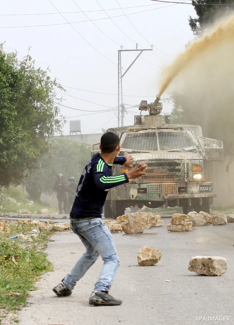 A Palestinian protester hurls stones toward An Israeli truck sprays foul smelling water during clashes with Israeli security forces following a demonstration against the expropriation of Palestinian land by Israel in the...