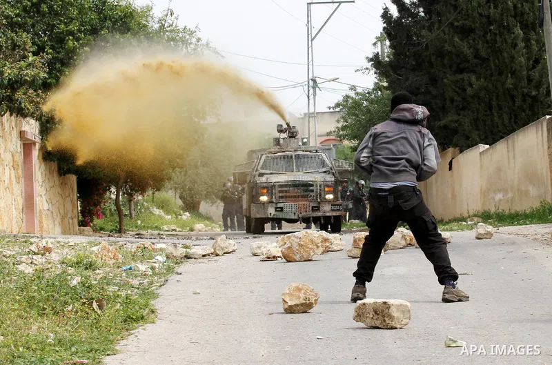 A Palestinian protester hurls stones toward An Israeli truck sprays foul smelling water during clashes with Israeli security forces following a demonstration against the expropriation of Palestinian land by Israel in the...