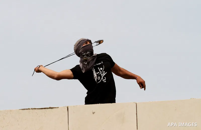 A Palestinian protester uses a slingshot to hurl stones toward Israeli security forces during clashes following a demonstration against the expropriation of Palestinian land by Israel in the village of Kfar Qaddum, near...