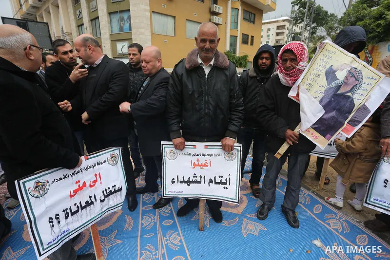Palestinian families of martyrs, hold banners during a protest to demand their salaries, in front of Red cross office, in Gaza city, on March 28, 2016. Photo by Mohammed Asad