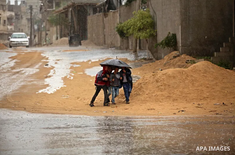 Palestinian students walk in a flooded street during a rainy day, in Khan Younis in the southern Gaza strip on March 28, 2016. Photo by Ashraf Amra