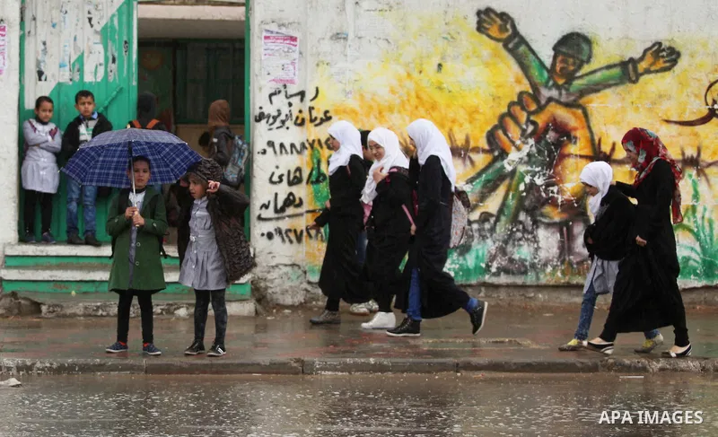 Palestinian students walk in a flooded street during a rainy day, in Khan Younis in the southern Gaza strip on March 28, 2016. Photo by Ashraf Amra