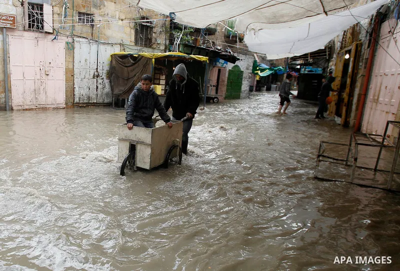 Palestinians walk in a street flooded by rain water in the West Bank city of Hebron, on March 28, 2016. Photo by Wisam Hashlamoun