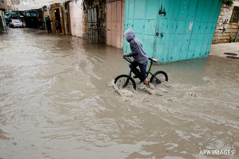 A Palestinian boy rides at a street flooded by rain water in the West Bank city of Hebron, on March 28, 2016. Photo by Wisam Hashlamoun