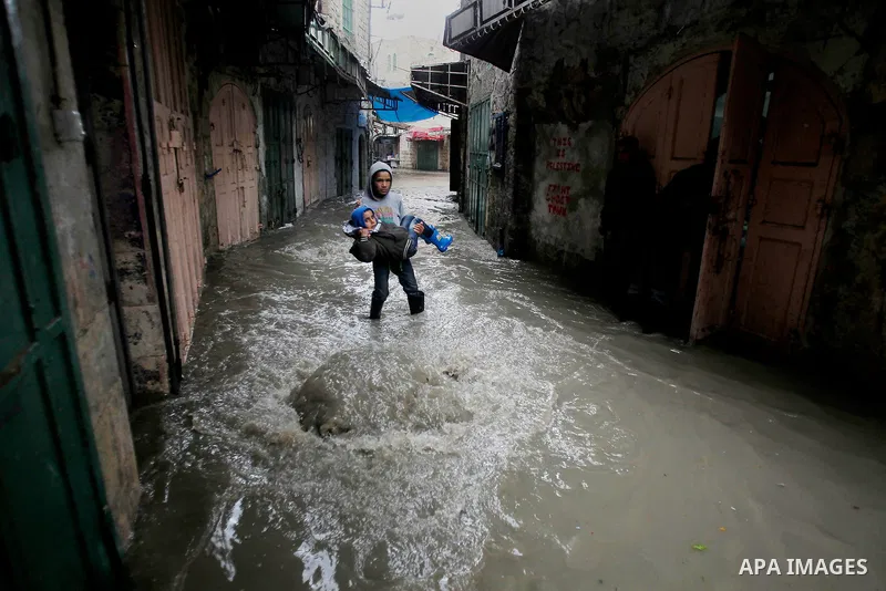 Palestinians walk in a street flooded by rain water in the West Bank city of Hebron, on March 28, 2016. Photo by Wisam Hashlamoun