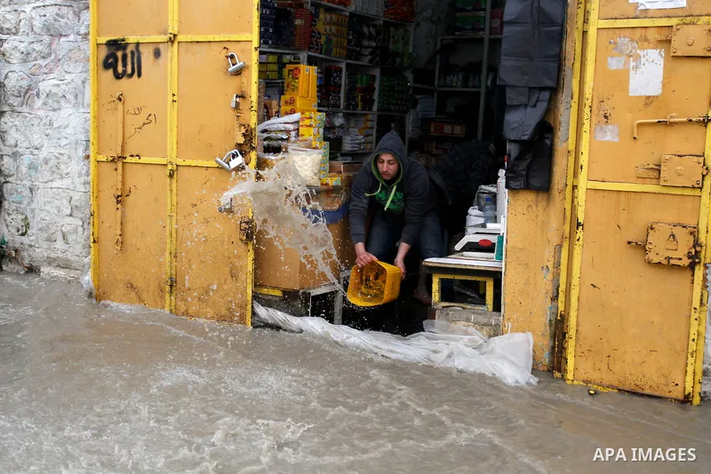 A Palestinian man cleans up flooded water outside his shop following heavy rains in the West Bank city of Hebron, on March 28, 2016. Photo by Wisam Hashlamoun