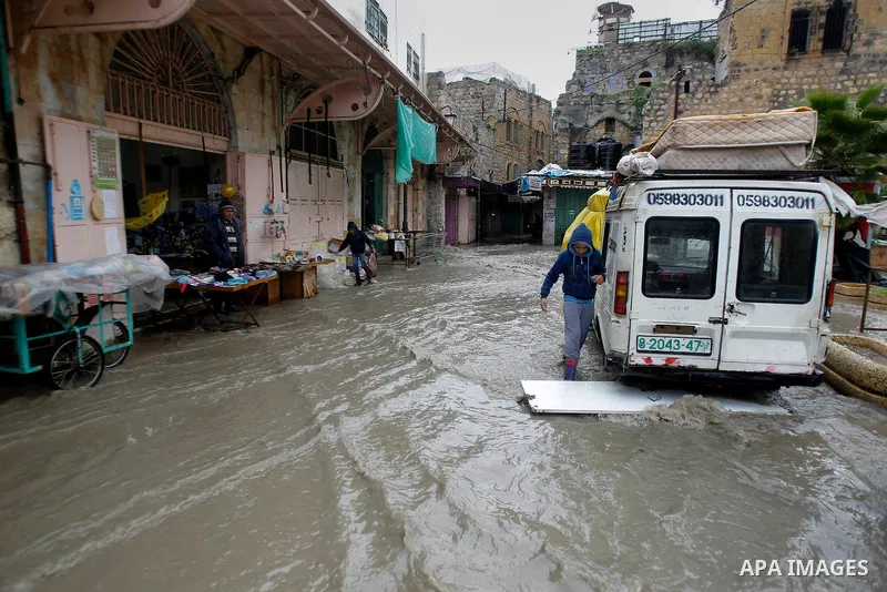 Palestinians walk in a street flooded by rain water in the West Bank city of Hebron, on March 28, 2016. Photo by Wisam Hashlamoun