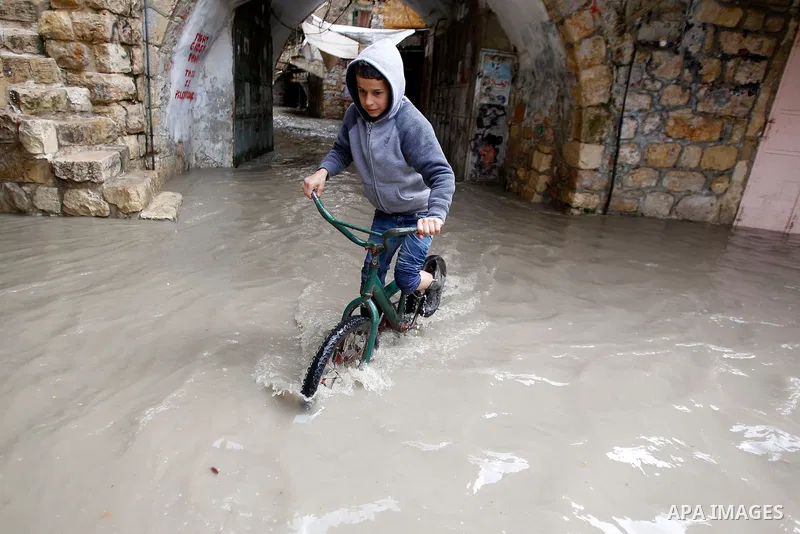 A Palestinian boy rides at a street flooded by rain water in the West Bank city of Hebron, on March 28, 2016. Photo by Wisam Hashlamoun