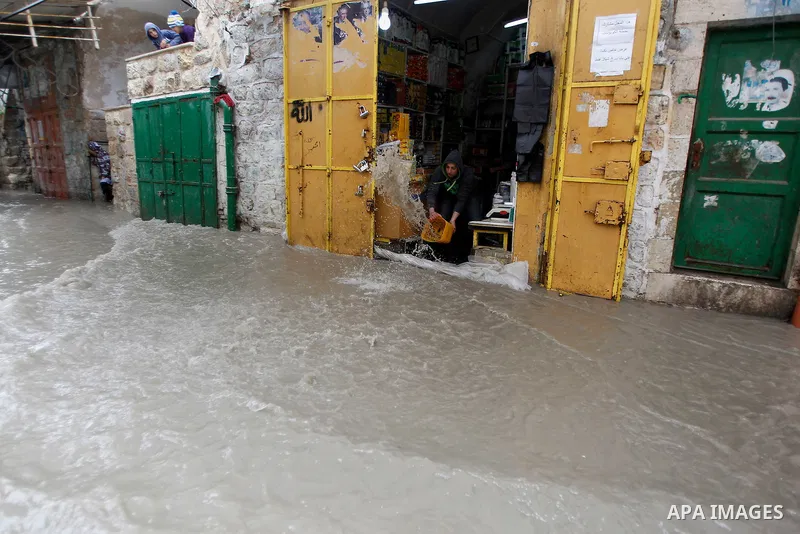A Palestinian man cleans up flooded water outside his shop following heavy rains in the West Bank city of Hebron, on March 28, 2016. Photo by Wisam Hashlamoun